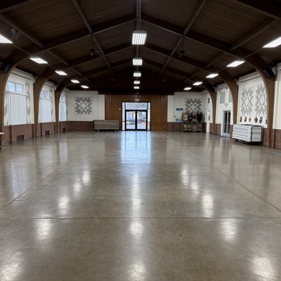 Interior view of a large, empty event hall with a high vaulted ceiling and polished concrete floor.