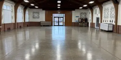 Interior view of a large, empty event hall with a high vaulted ceiling and polished concrete floor.