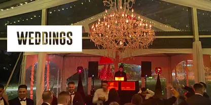 Wedding reception with a DJ at a booth, chandelier lighting, and guests dancing on the floor.