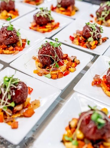 A tray of plated appetizers featuring meatballs served over a vegetable base, garnished with microgreens.