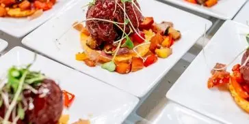 A tray of plated appetizers featuring meatballs served over a vegetable base, garnished with microgreens.