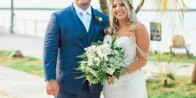A bride and groom standing on a sandy beach with palm trees in the background.