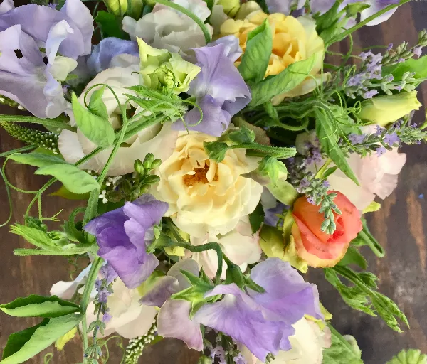 Close-up photograph of a fresh floral arrangement with yellow roses, purple sweet peas, and greenery.