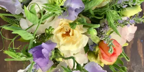 Close-up photograph of a fresh floral arrangement with yellow roses, purple sweet peas, and greenery.