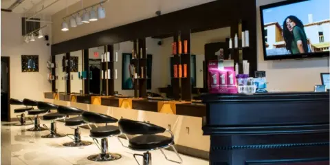 Interior of a hair salon with black styling chairs, mirrors, and shelves of hair products.