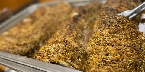 A large, herb-crusted meatloaf sliced and served in a stainless steel catering tray.