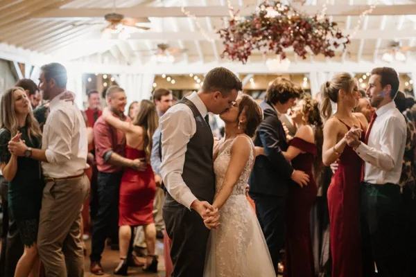 A bride and groom sharing a first dance at a wedding reception while guests watch and dance around them.