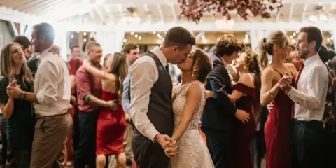 A bride and groom sharing a first dance at a wedding reception while guests watch and dance around them.