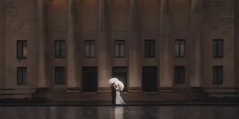 A bride and groom kissing under a white umbrella in front of the William Rockhill Nelson Gallery of Art.