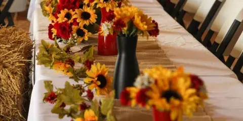 A rustic wedding reception table set with a burlap runner, white chairs, and sunflower centerpieces inside a timber barn.