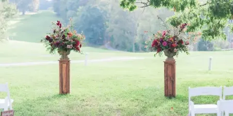 Outdoor wedding ceremony aisle decorated with wooden pedestals and floral arrangements on a grassy lawn.