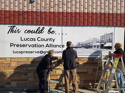 Workers installing a Lucas County Preservation Alliance banner on a historic brick building.
