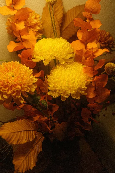 A close-up of a floral arrangement with yellow chrysanthemums and orange autumn leaves.