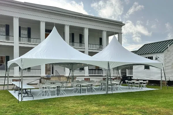 White event tents set up on a lawn with tables and chairs arranged underneath.