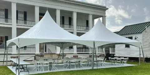 White event tents set up on a lawn with tables and chairs arranged underneath.
