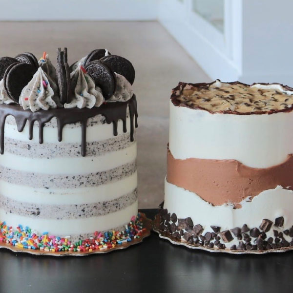 Two decorated cakes, one with chocolate drip and Oreo toppings, and another with a semi-naked style and chocolate chunks, displayed on a table.