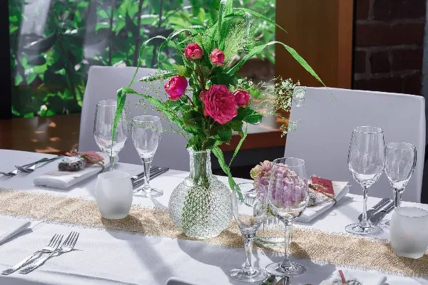A decorated event table with white linens, glassware, flatware, and a floral centerpiece.