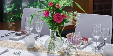 A decorated event table with white linens, glassware, flatware, and a floral centerpiece.