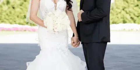 A groom in a black tuxedo and bow tie standing next to a bride in a white wedding dress.
