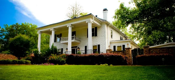 Exterior view of a white two-story historic home with a columned porch and manicured lawn.