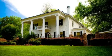 Exterior view of a white two-story historic home with a columned porch and manicured lawn.