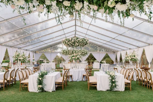 Interior of a wedding reception tent featuring white tablecloths, floral centerpieces, and hanging floral installations.