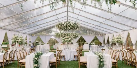 Interior of a wedding reception tent featuring white tablecloths, floral centerpieces, and hanging floral installations.