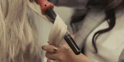 A close-up of a hairstylist using a curling iron to style a client's long blonde hair.