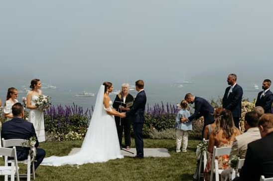 A wedding ceremony taking place outdoors with an officiant standing between the bride and groom.