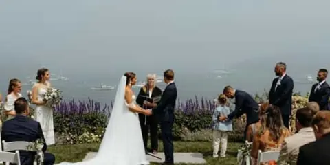 A wedding ceremony taking place outdoors with an officiant standing between the bride and groom.