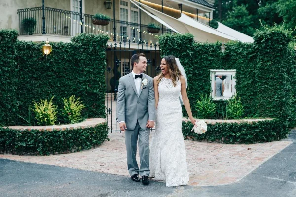 A bride and groom standing together in a courtyard with manicured hedges and a building entrance.