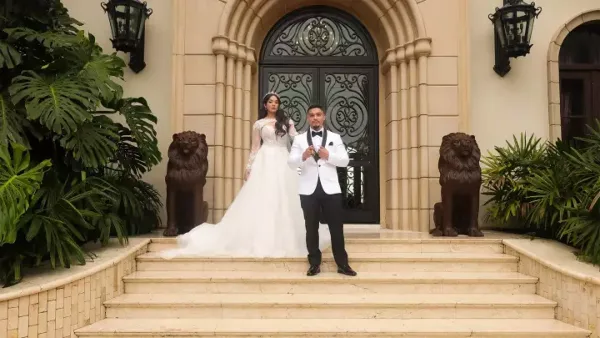 A bride in a white gown and a groom in a tuxedo standing on the steps of a grand building entrance.