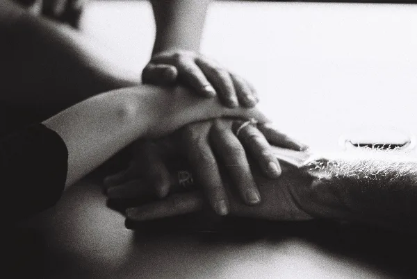 Black-and-white close-up of multiple hands stacked together, one wearing a ring.