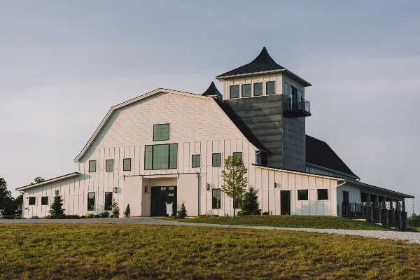Exterior view of a large white barn-style building with a black metal tower and cupola, set on a grassy lawn.