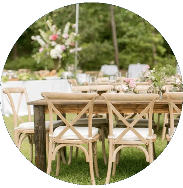 Outdoor event setup featuring rustic wooden cross-back chairs and a farmhouse table on a lawn.