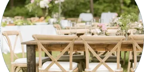 Outdoor event setup featuring rustic wooden cross-back chairs and a farmhouse table on a lawn.