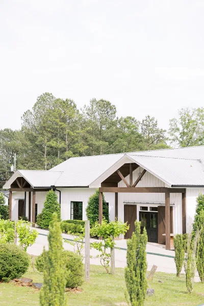 Exterior view of a white barn wedding venue with a wooden pavilion and surrounding greenery.