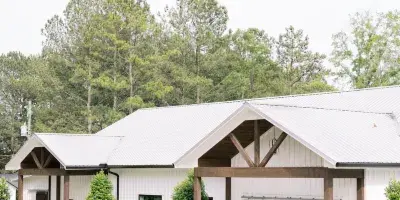Exterior view of a white barn wedding venue with a wooden pavilion and surrounding greenery.