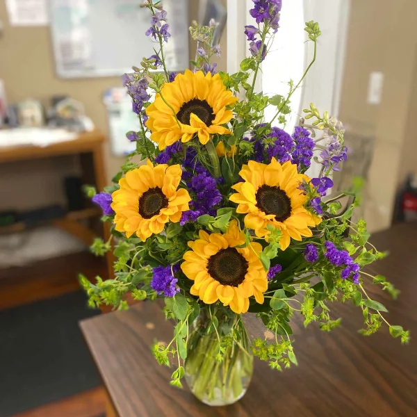 A floral arrangement featuring yellow sunflowers and purple flowers in a clear glass vase.