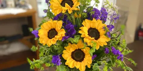 A floral arrangement featuring yellow sunflowers and purple flowers in a clear glass vase.