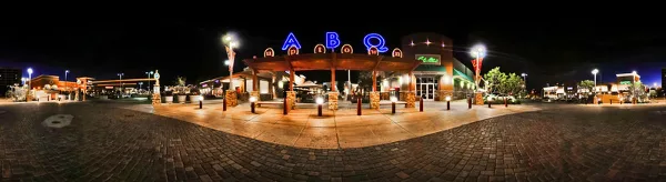 Wide-angle night photograph of a building exterior with illuminated 'ABQ' signage and a cobblestone plaza.
