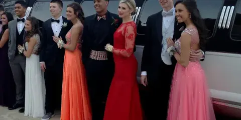 A group of formally dressed young adults posing with a black limousine.