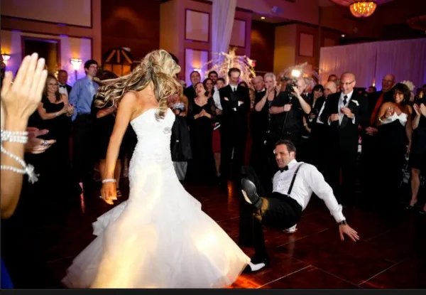 A bride and groom dancing at a wedding reception while guests applaud.
