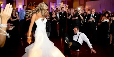 A bride and groom dancing at a wedding reception while guests applaud.