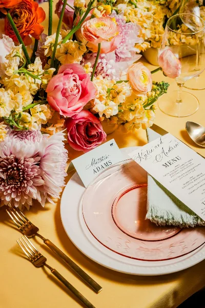 A close-up of a formal dining table setting featuring a menu card, place card, and floral centerpiece.