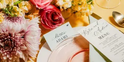 A close-up of a formal dining table setting featuring a menu card, place card, and floral centerpiece.