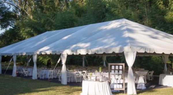 A large white event tent set up on a lawn with tables and chairs for an outdoor reception.