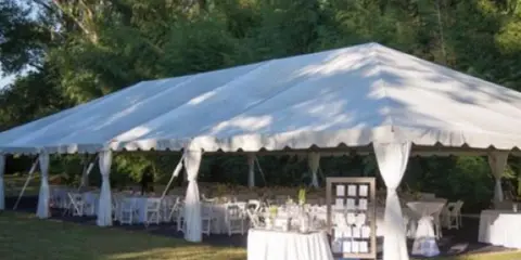 A large white event tent set up on a lawn with tables and chairs for an outdoor reception.