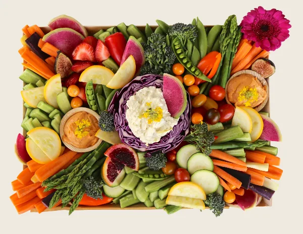 A top-down view of a catering crudité board filled with arranged vegetables, fruit, and dips.
