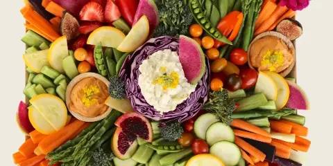 A top-down view of a catering crudité board filled with arranged vegetables, fruit, and dips.